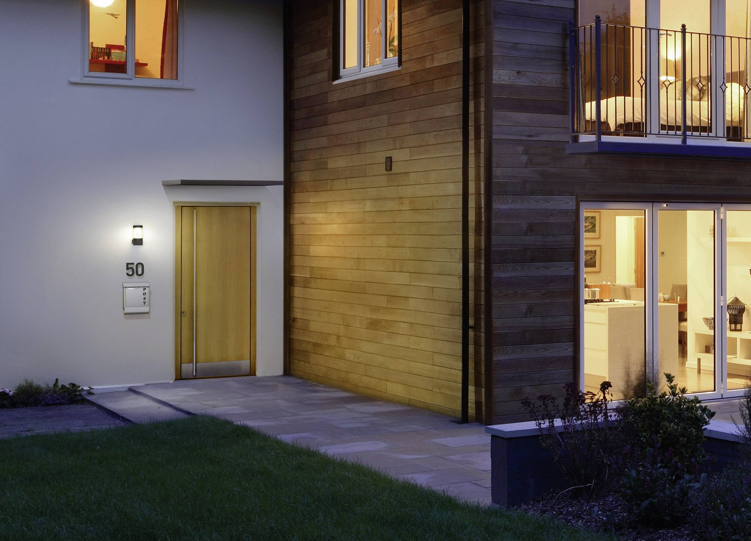 Ein modernes zweistöckiges Haus bei Dämmerung mit großer Glasfront, beleuchtetem Eingang und Holzwandverkleidung.