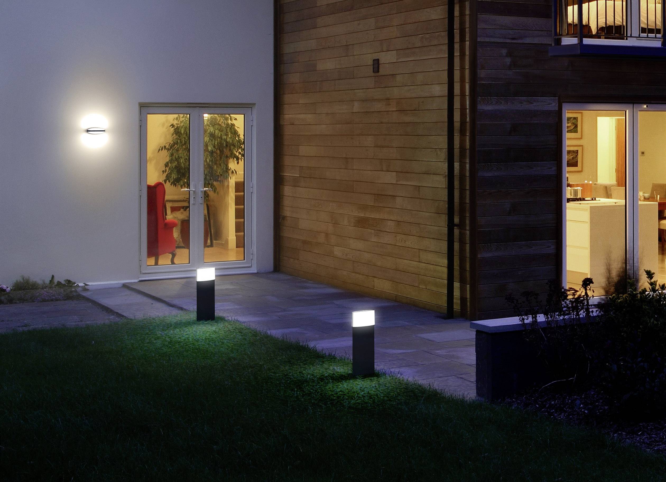 Wohnhaus mit beleuchtetem Garten in der Nacht; Licht strahlt aus den Fenstern und zwei Gartenleuchten beleuchten den Pflanzenbereich.