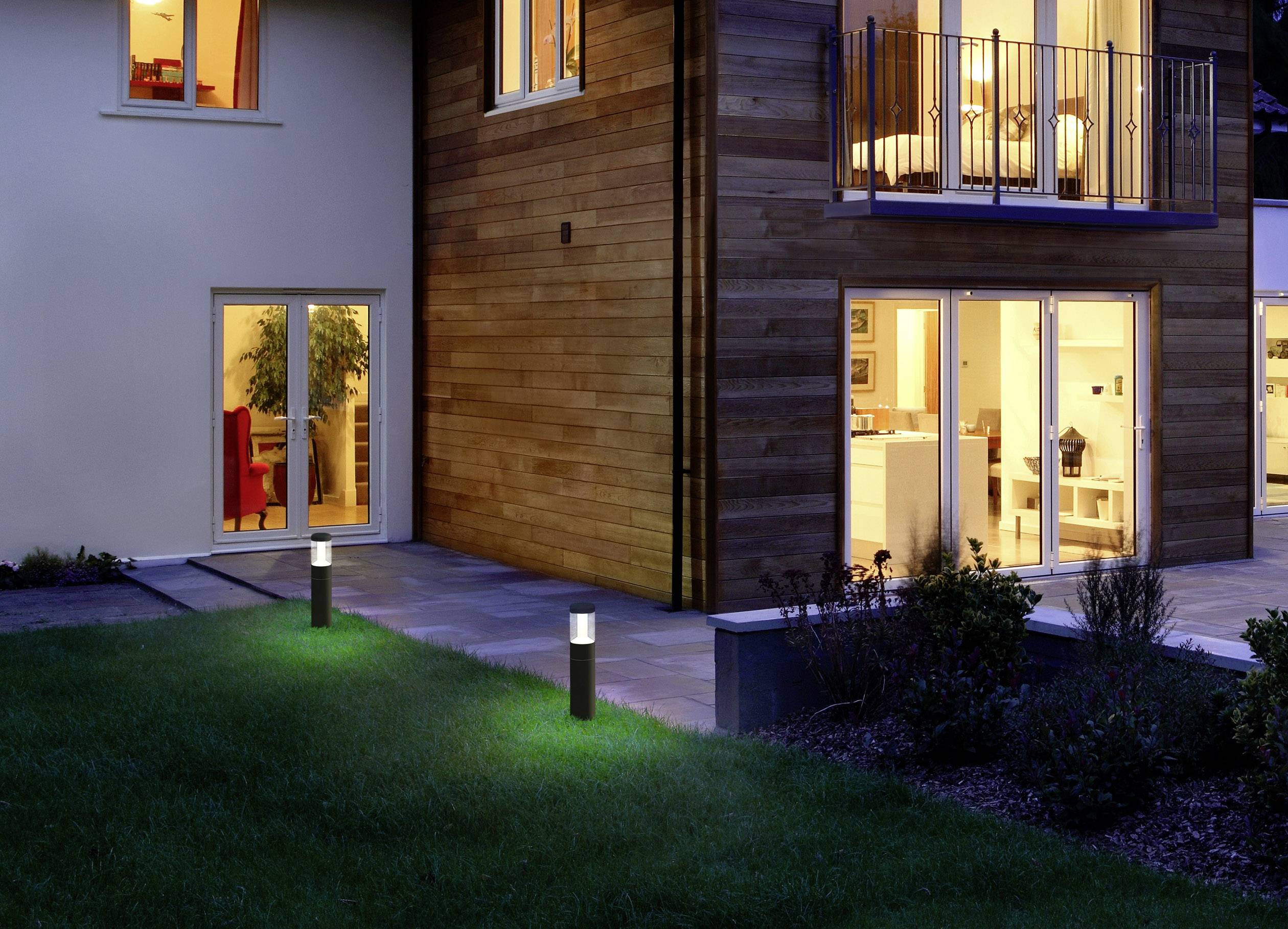 Ein modernes Haus bei Nacht mit beleuchtetem Innenraum und Gartenleuchten. Große Fenster geben Einblick ins Wohnzimmer.
