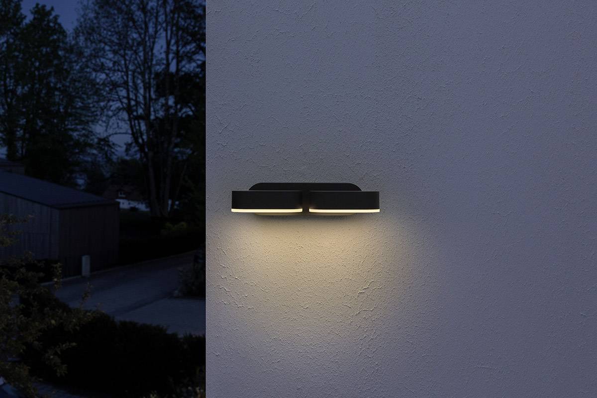 Eine moderne Außenlampe leuchtet an einer Hauswand in der Dämmerung.