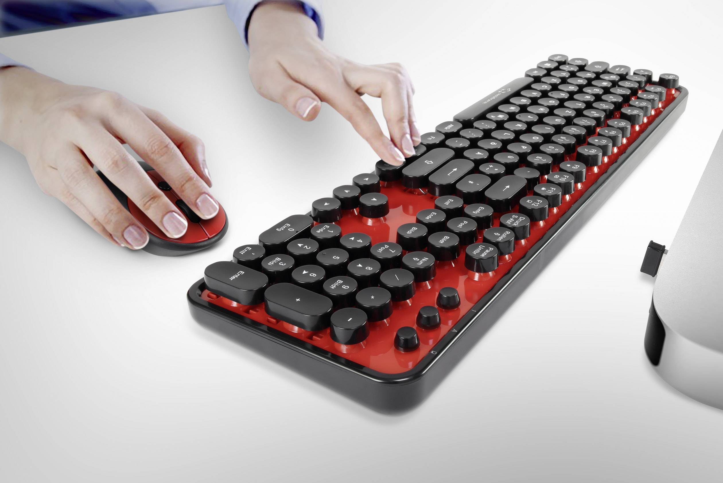 'Eine Person tippt auf einer rot-schwarzen Retro-Tastatur und benutzt eine computermaus auf einem weißen Tisch.'