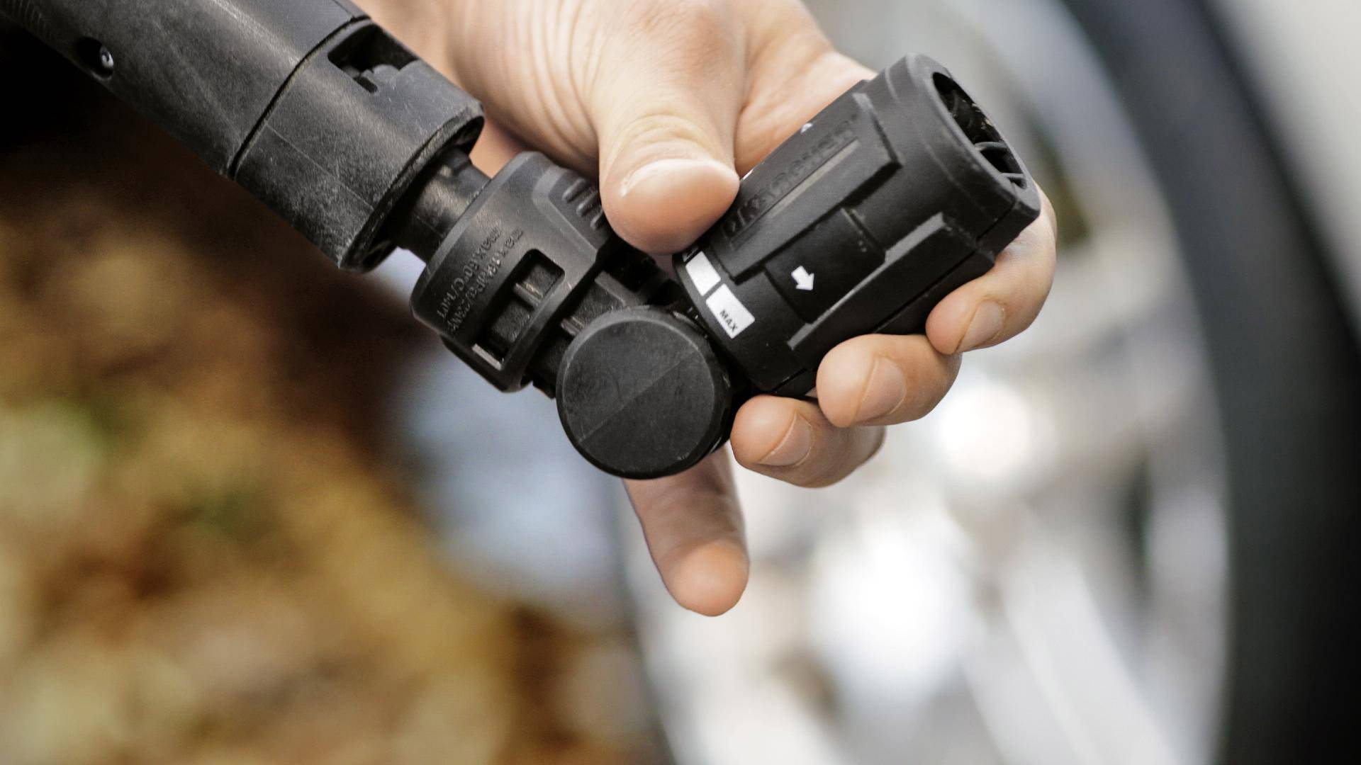 Hand hält einen Autoladestecker, der bereit zum Anschließen ist, mit einem verschwommenen Hintergrund eines Autoreifens.