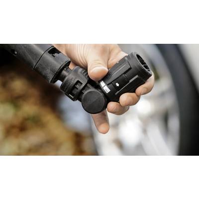 Hand hält einen Autoladestecker, der bereit zum Anschließen ist, mit einem verschwommenen Hintergrund eines Autoreifens.