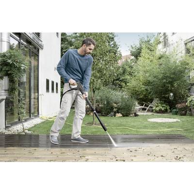Ein Mann reinigt mit einem Hochdruckreiniger eine Terrasse. Im Hintergrund sind Pflanzen und ein Haus zu sehen.