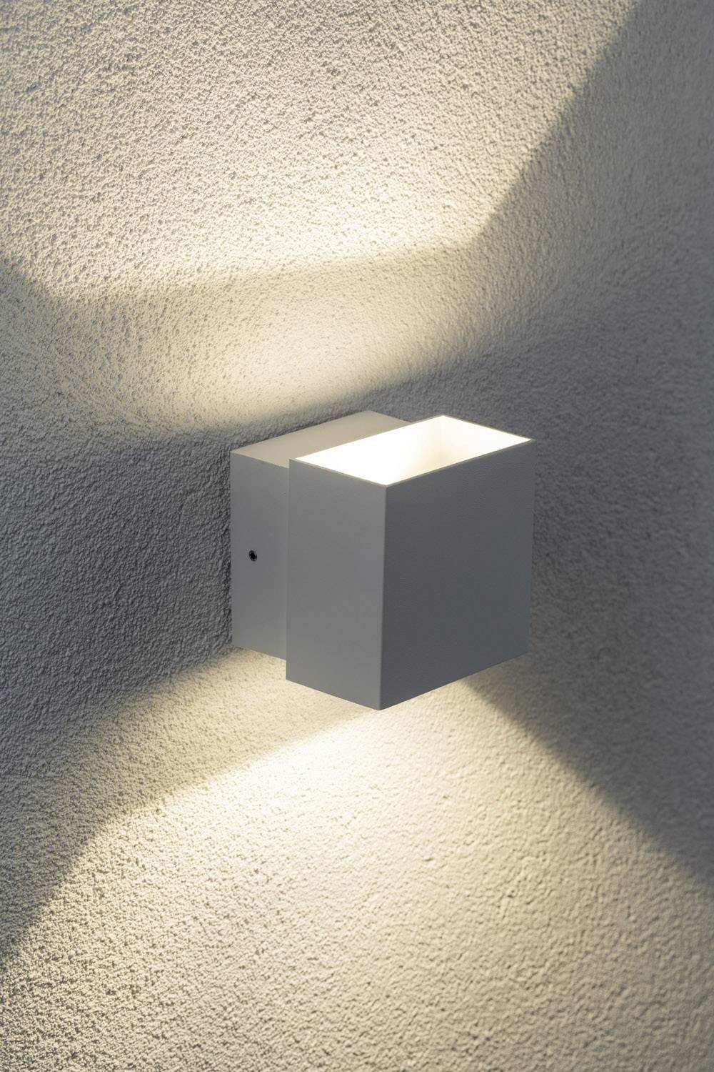 Weiße Wandleuchte in Würfelform, die nach oben und unten Lichtkegel auf eine graue Wand wirft.