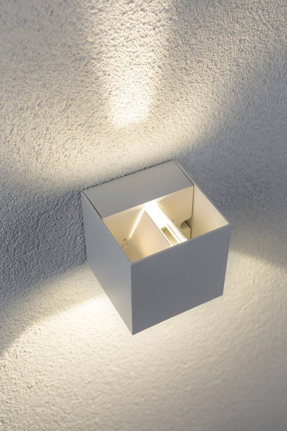 Eine moderne Wandleuchte mit einem minimalistischen, quadratischen Design strahlt weiches Licht nach oben und unten auf eine Wand.