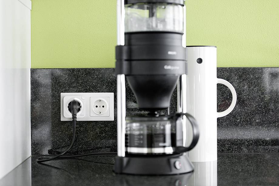 Eine Filterkaffeemaschine steht auf einer Küchenarbeitsplatte neben einer Steckdose. Daneben ist eine weiße Thermoskanne.