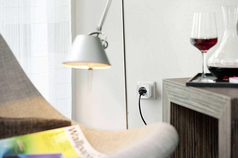 Ein gemütlicher Wohnbereich mit einem modernen Stuhl, Leselampe, einem Tisch mit Rotweinglas und Karaffe, und einer Steckdose an der Wand.