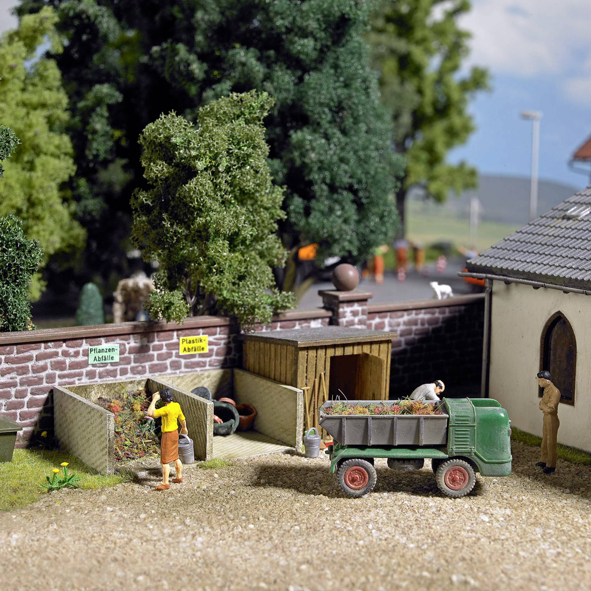 Miniaturszene eines Bauernhofs mit zwei Personen. Eine Person füttert Tiere, die andere belädt einen Anhänger mit Pflanzen. Im Hintergrund sind Bäume.