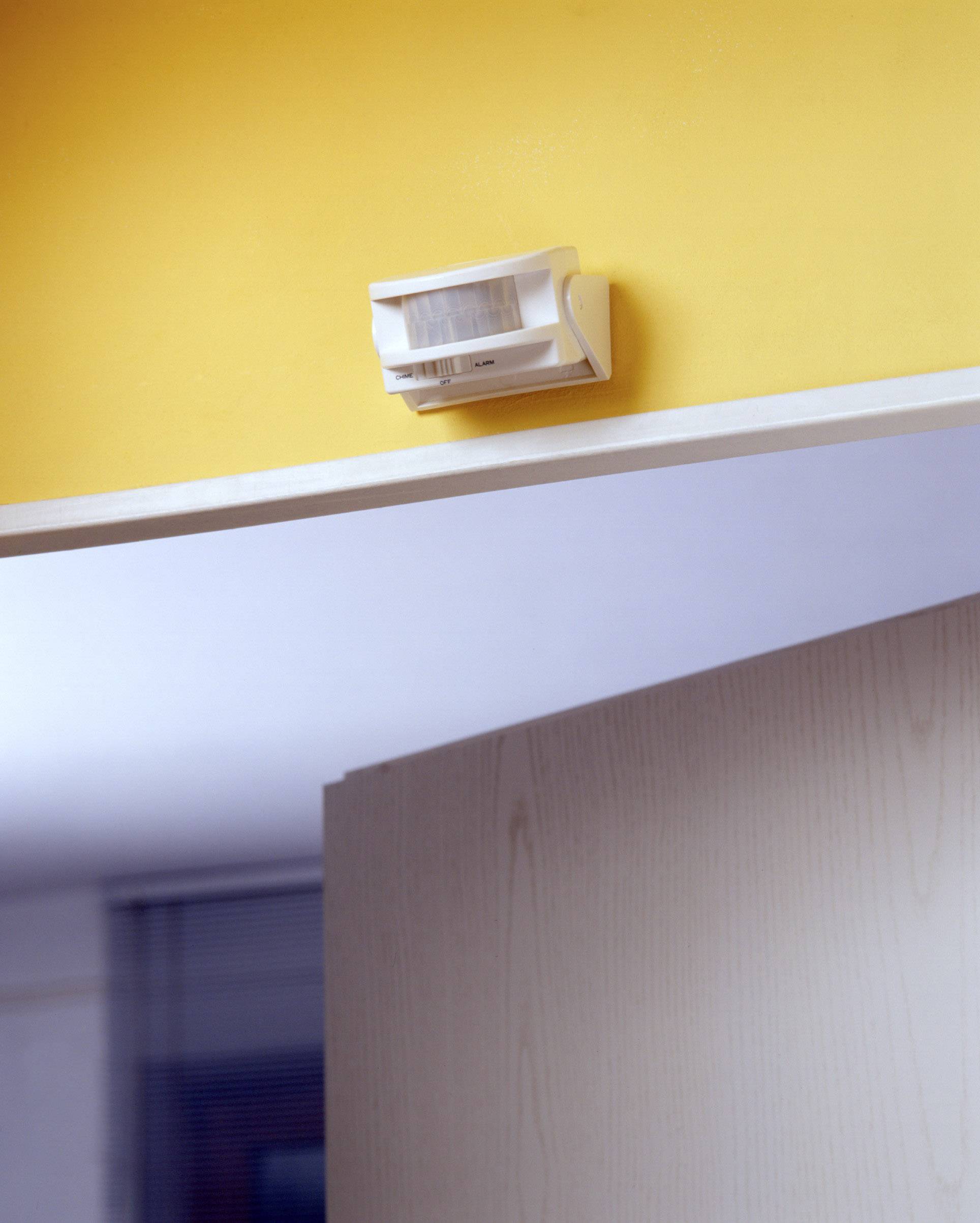 Ein Bewegungsmelder ist an einer gelben Wand über einer offenen Tür montiert, bereit zur Erfassung von Bewegung im Raum.