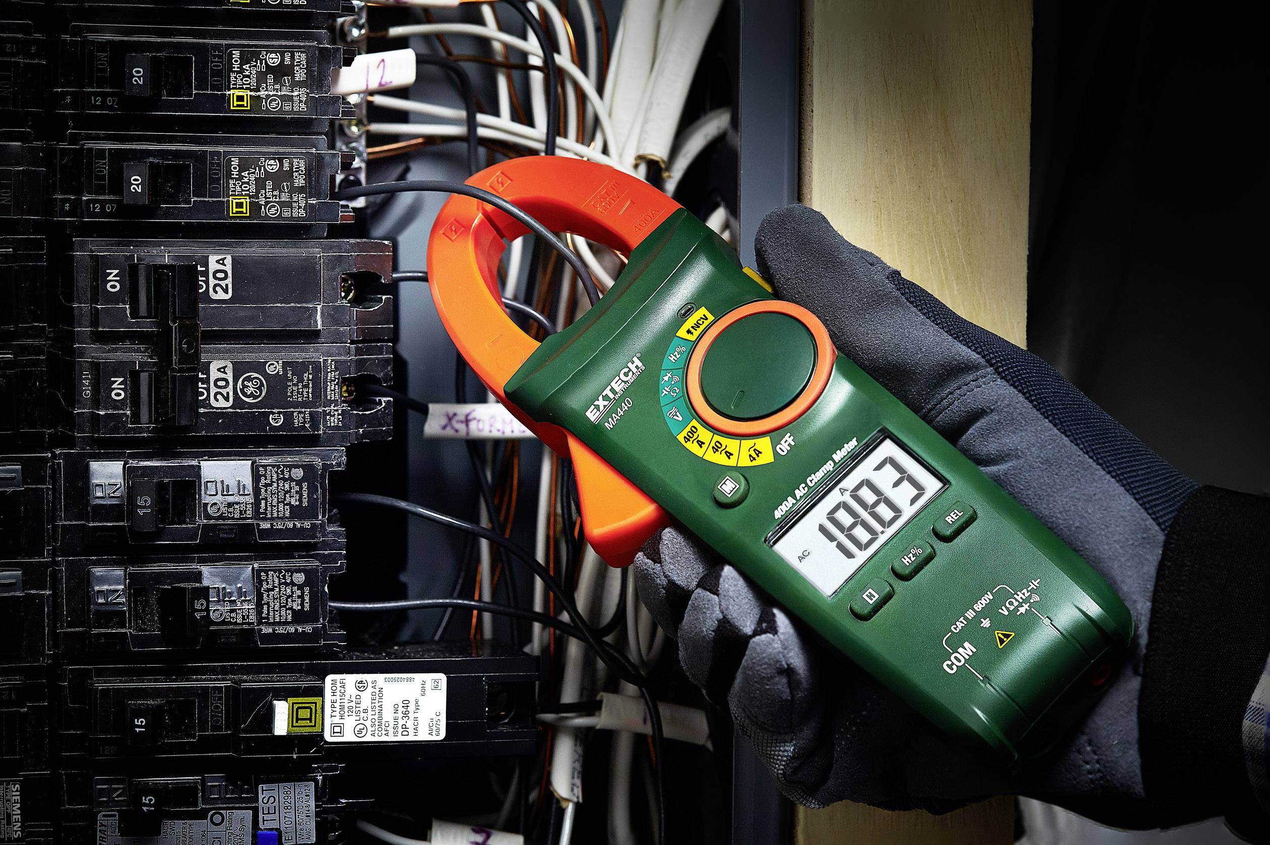 Eine Person hält ein digitales Amperemeter im Handschuh. Es misst den Stromkreis bei 188,3 Ampere. Im Hintergrund sind Sicherungen sichtbar.