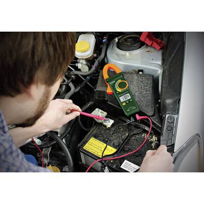 'Ein Mann überprüft mit einem Multimeter die Spannung einer Autobatterie im Motorraum. Das Gerät zeigt 12.84 Volt an.'