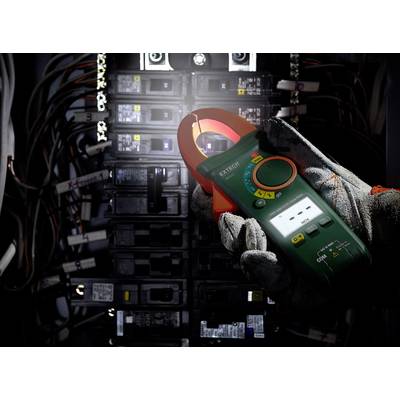 Ein Elektriker hält ein Strommessgerät vor einem geöffneten Schaltschrank mit mehreren Sicherungen und Kabeln.