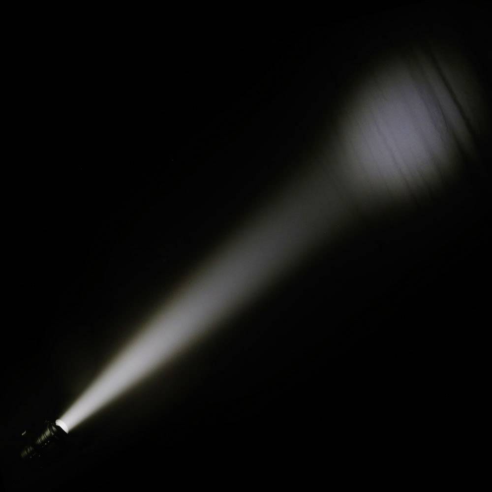 Eine Taschenlampe strahlt einen fokussierten Lichtkegel in einem dunklen Raum aus, der einen klaren Kreis an der Wand bildet.