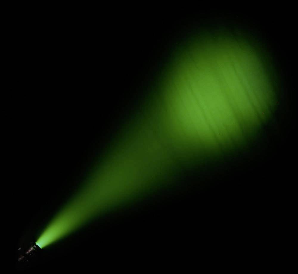 Ein grüner Scheinwerferstrahl leuchtet in die Dunkelheit, erzeugt einen breiten Lichtkegel.
