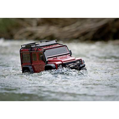 Ein rotes Modellauto eines Geländewagens fährt durch flaches Wasser, umgeben von fließendem Fluss.
