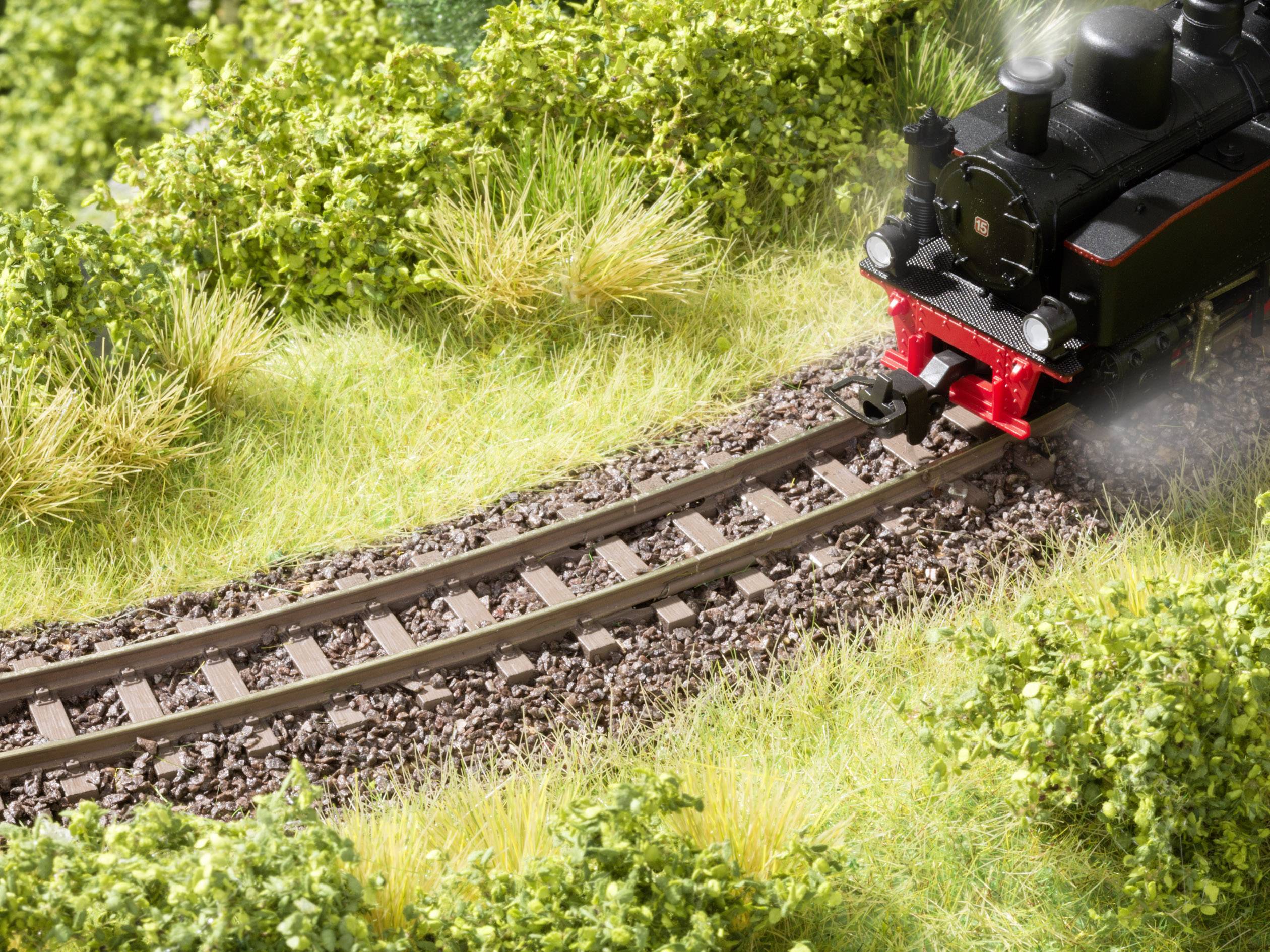 Eine kleine schwarze Dampflok fährt auf einer Modelleisenbahnstrecke in einer grünen, bewachsenen Landschaft.