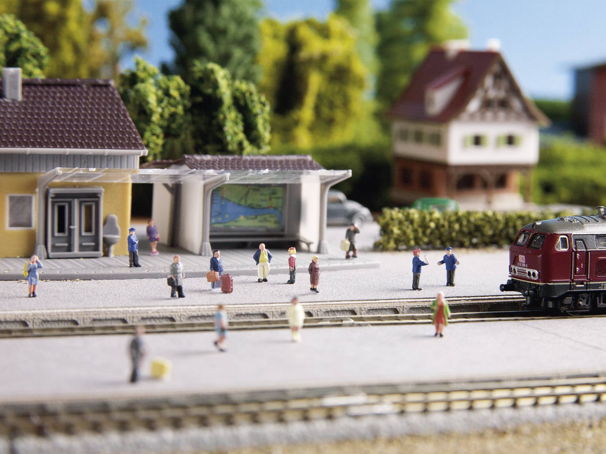 Miniaturbahnhof mit wartenden Miniaturfiguren, Zug und umliegenden Häusern zeigt eine realistische Szene eines ländlichen Bahnhofs.