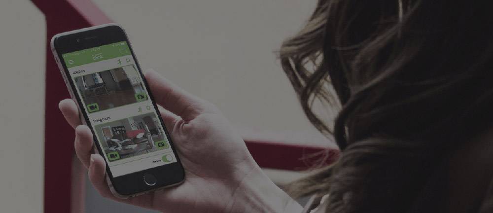 Eine Person hält ein Smartphone in der Hand, auf dem eine App mit Bildern von verschiedenen Zimmern angezeigt wird.