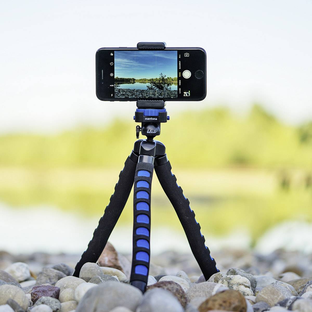 Ein Smartphone auf einem kleinen Stativ, das eine Landschaft mit einem Fluss im Hintergrund aufnimmt. Das Bild fokussiert auf Technik.