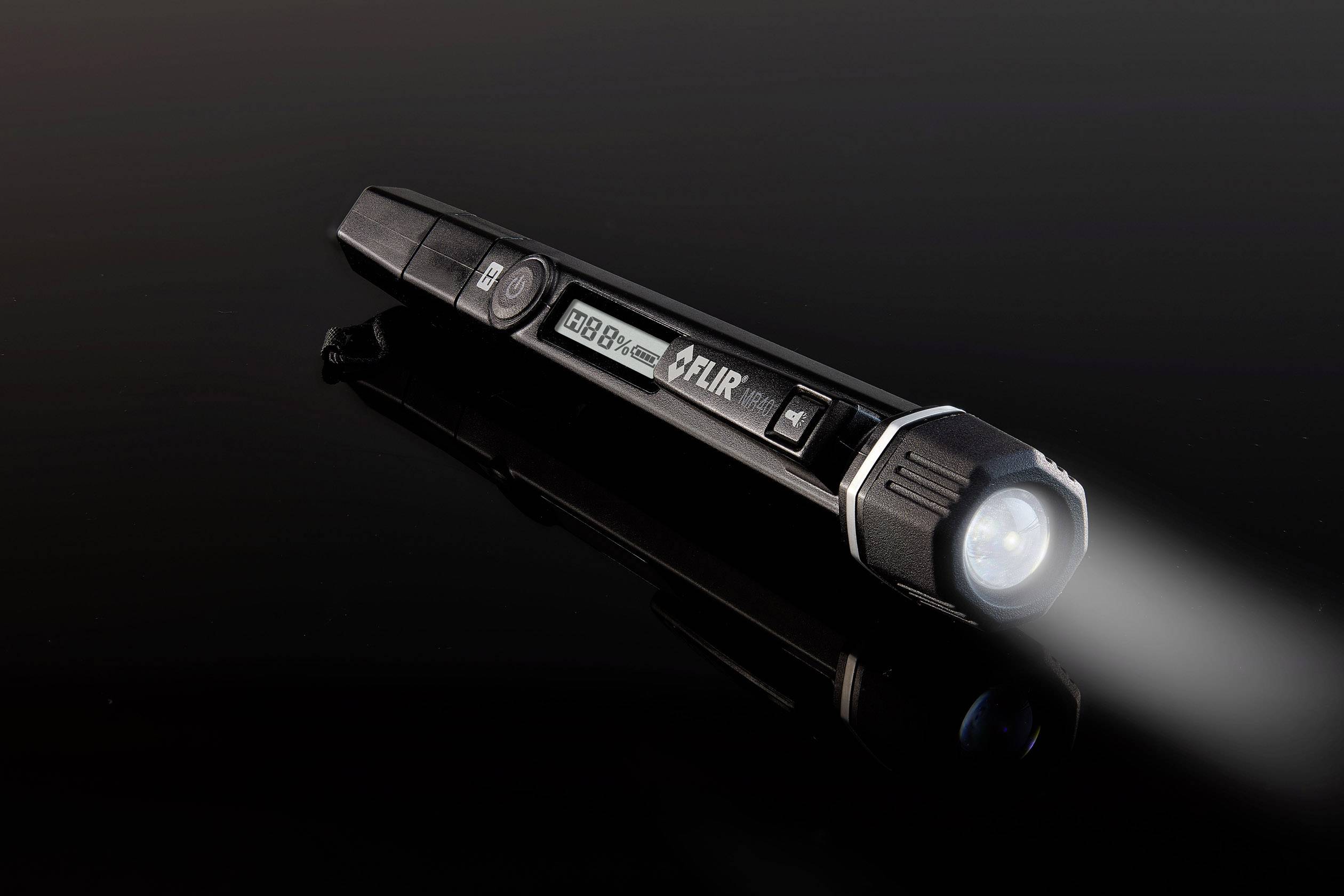 Eine schwarze Taschenlampe leuchtet auf einer dunklen Oberfläche; das Licht strahlt nach rechts.