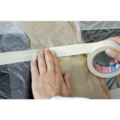 Eine Person klebt Kreppband auf eine Plastikfolie, um Oberflächen zu schützen, wahrscheinlich beim Malen oder Renovieren.