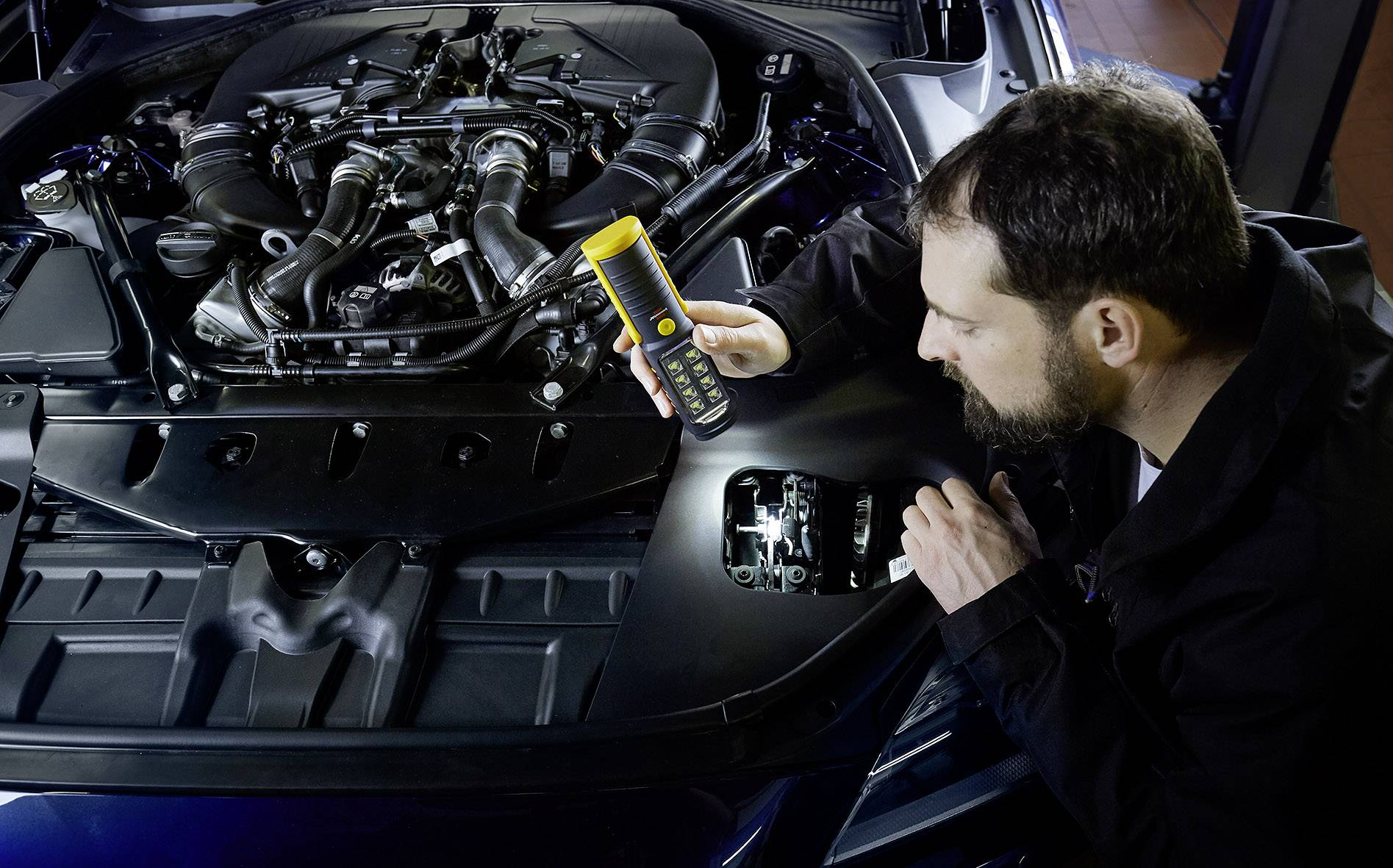 Ein Mann überprüft mit einem digitalen Messgerät die Motorleistung eines Autos, während die Motorhaube geöffnet ist.