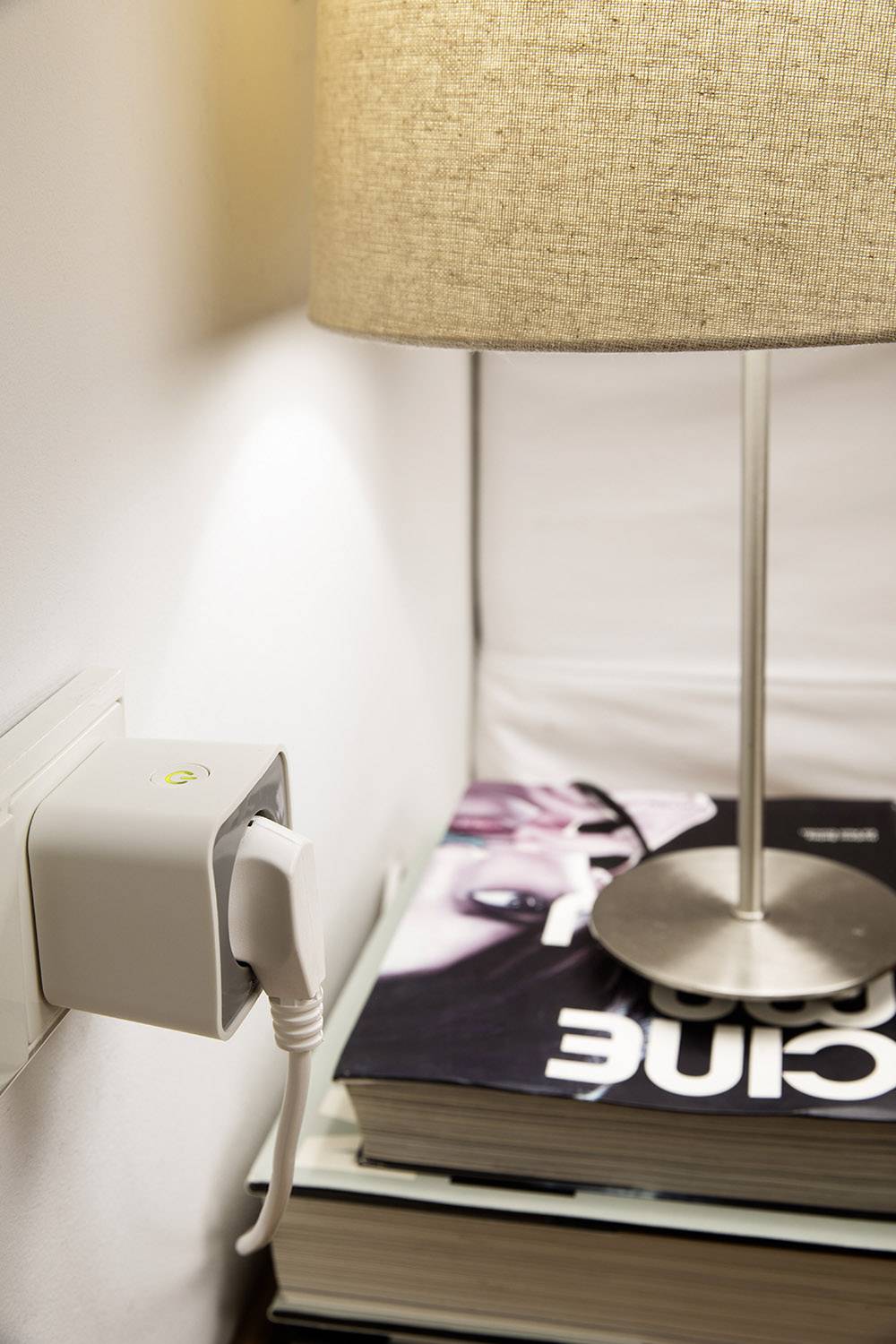 Lampe auf einem Nachttisch, angeschlossen an eine Steckdose mit einem Smart-Stecker, auf einem Stapel Zeitschriften.