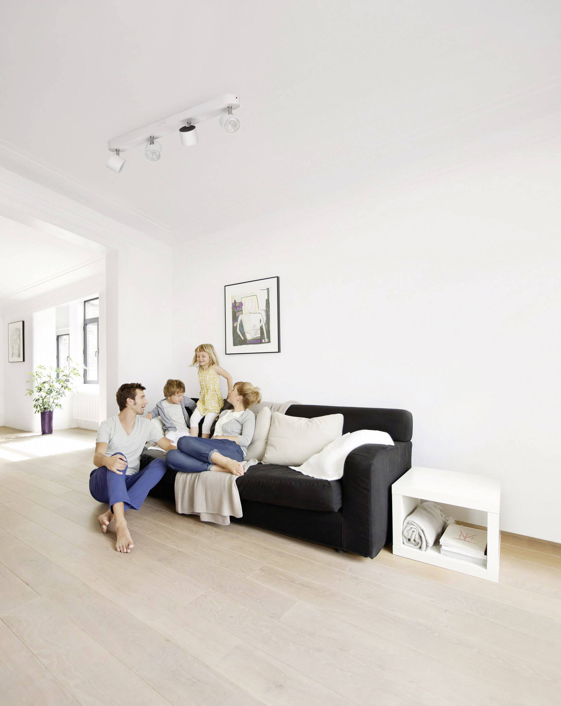 Eine Familie mit zwei Kindern sitzt entspannt auf einem Sofa in einem hellen Wohnzimmer. Eine Pflanze steht im Hintergrund.