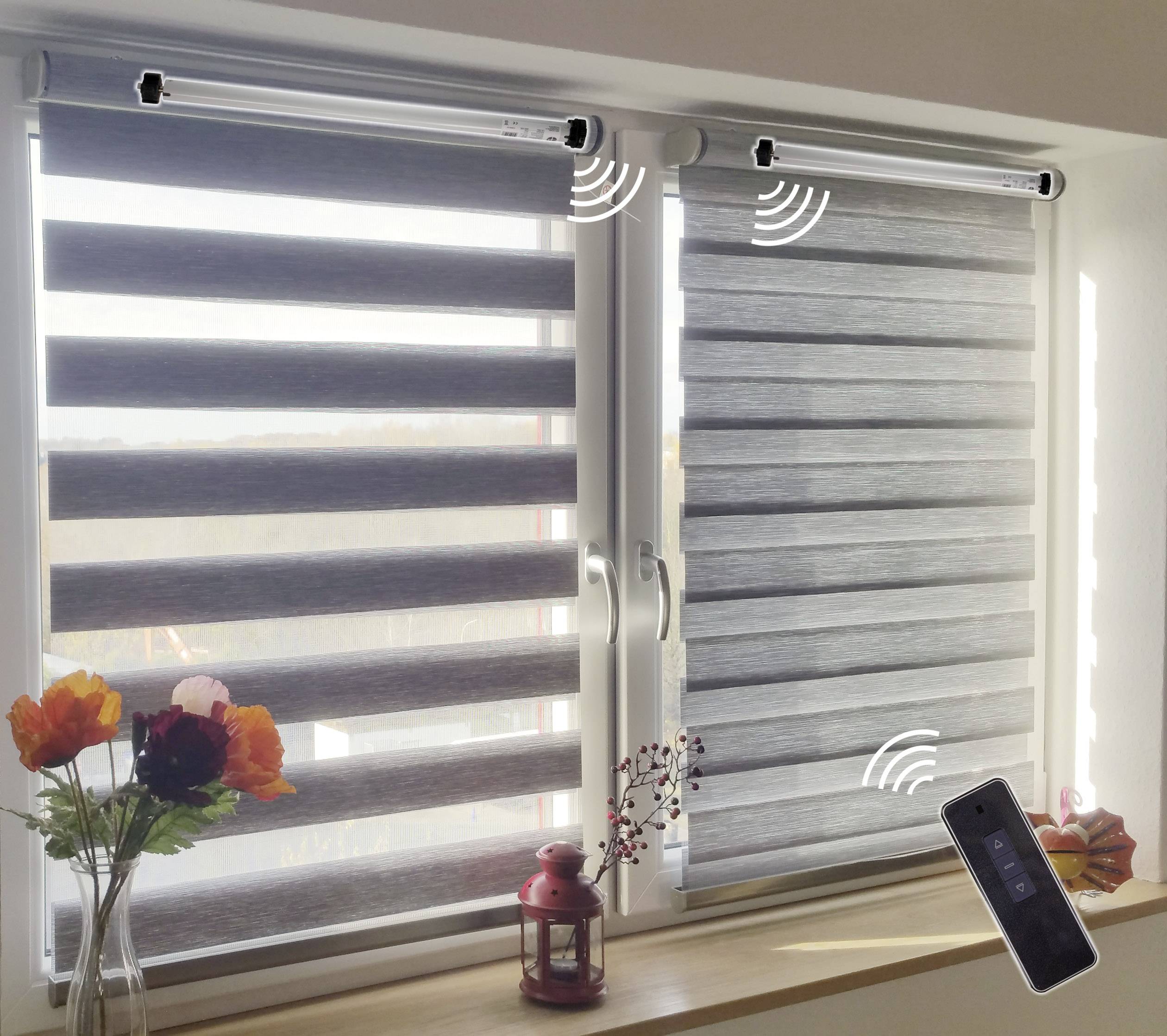 Zwei Fenster mit motorisierten Jalousien, die per Fernbedienung gesteuert werden können. Auf der Fensterbank stehen Blumen und eine Laterne.