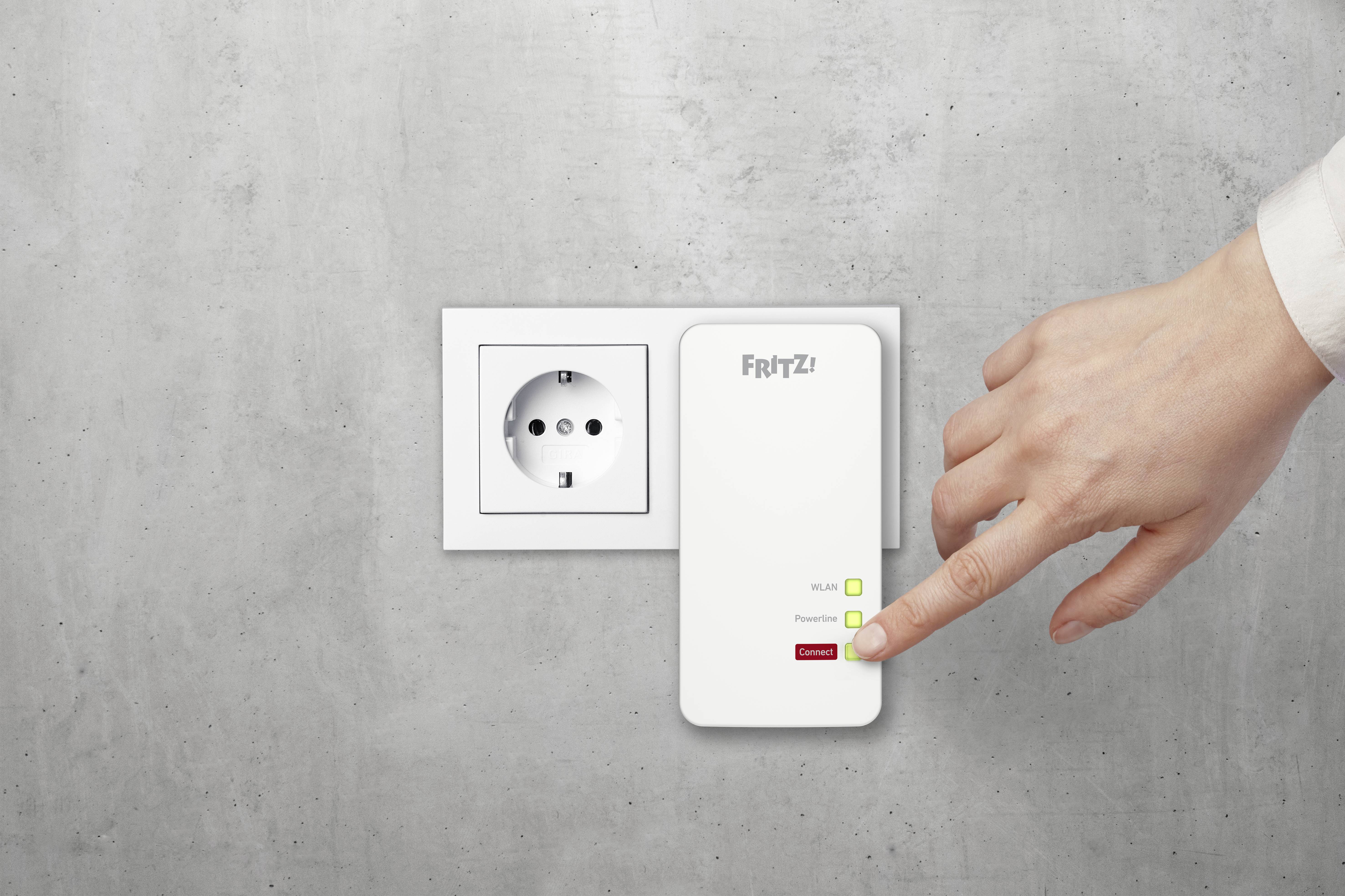Eine Hand betätigt den Schalter eines FRITZ! WLAN Repeaters, der in eine Steckdose an einer grauen Wand gesteckt ist.