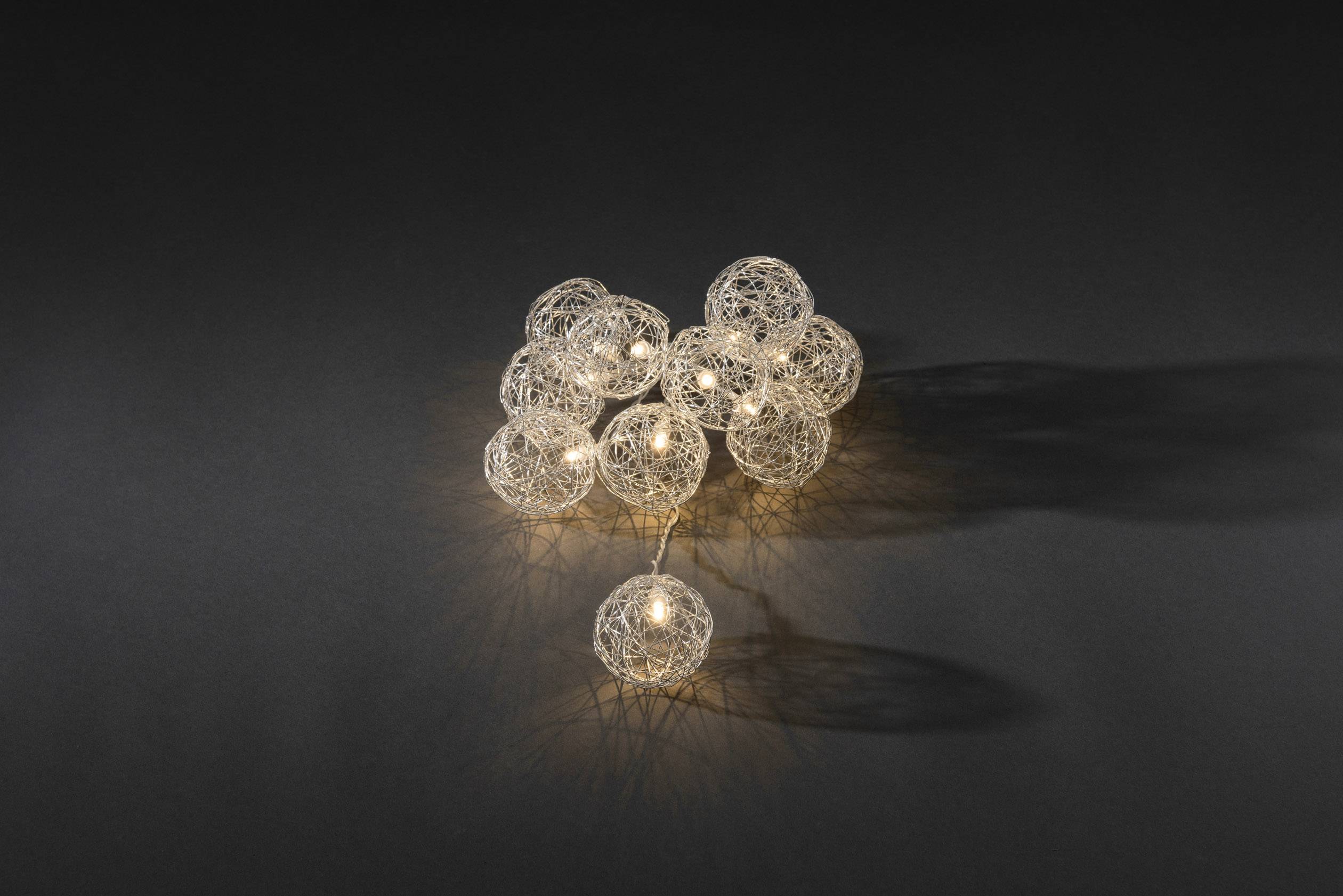 Mehrere kugelförmige Lampen mit filigranem Drahtdesign strahlen auf dunklem Hintergrund, werfen sanfte, sich überschneidende Schatten.