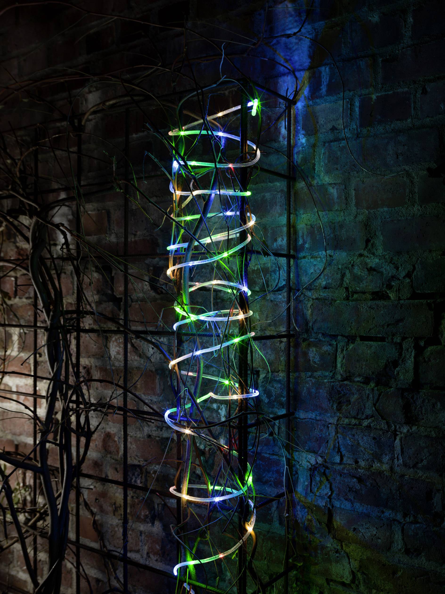 Ein Metallgitter an einer Backsteinwand ist mit bunten, leuchtenden Lichtern umwickelt, die eine spiralförmige Anordnung bilden.
