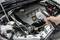 Ein Automechaniker misst mit einem Infrarot-Thermometer die Temperatur eines Motors, der in einem offenen Motorraum eines Autos zu sehen ist.