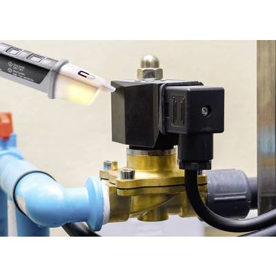 Ein blaues Rohr mit einem goldfarbenen Ventil und einem schwarzen elektrischen Bauteil verbunden. Eine Hand hält ein Prüfgerät an das Ventil.