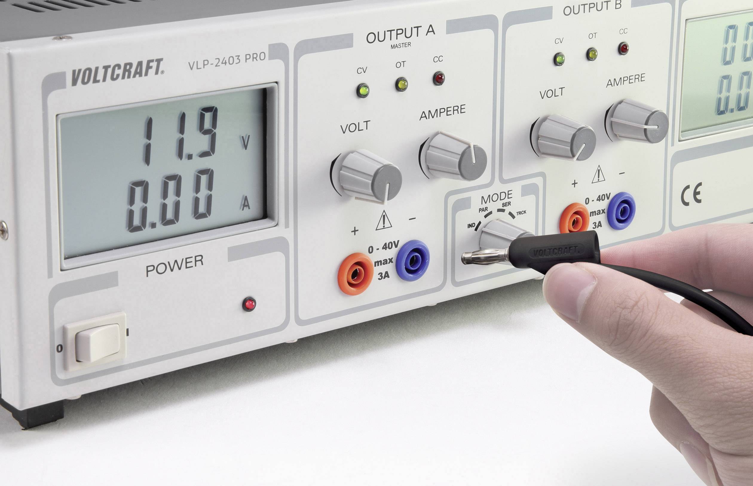 Elektronisches Netzteil mit Anzeige von '11,9 V' und '0,00 A'. Ein Hand hält eine Messsonde, die an den Ausgang A angeschlossen werden soll.