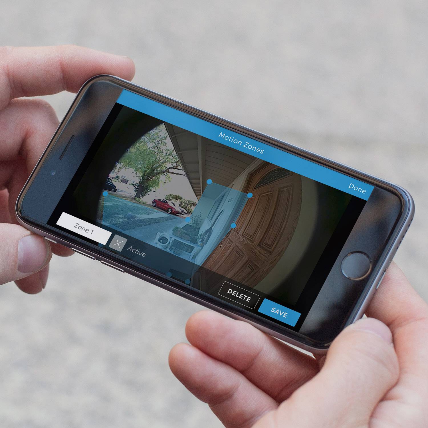 Eine Person hält ein Smartphone mit einer App zur Überwachung von Bewegungszonen an einer Eingangstür.