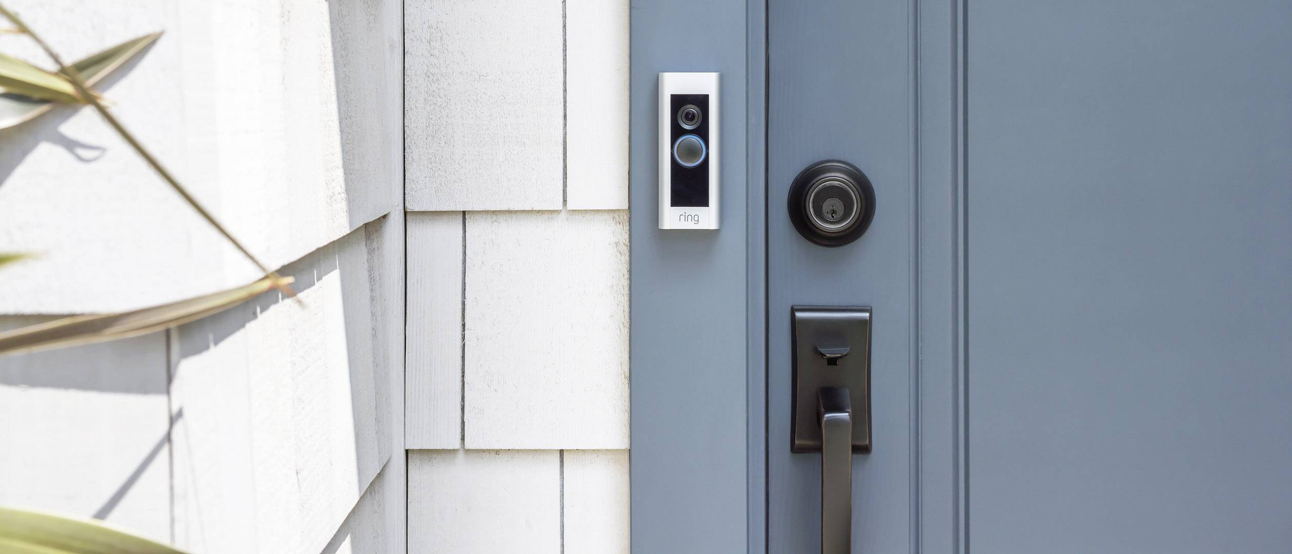 Das Bild zeigt eine blaue Haustür mit einem Türgriff. Daneben befindet sich eine Türklingel mit Kamera.