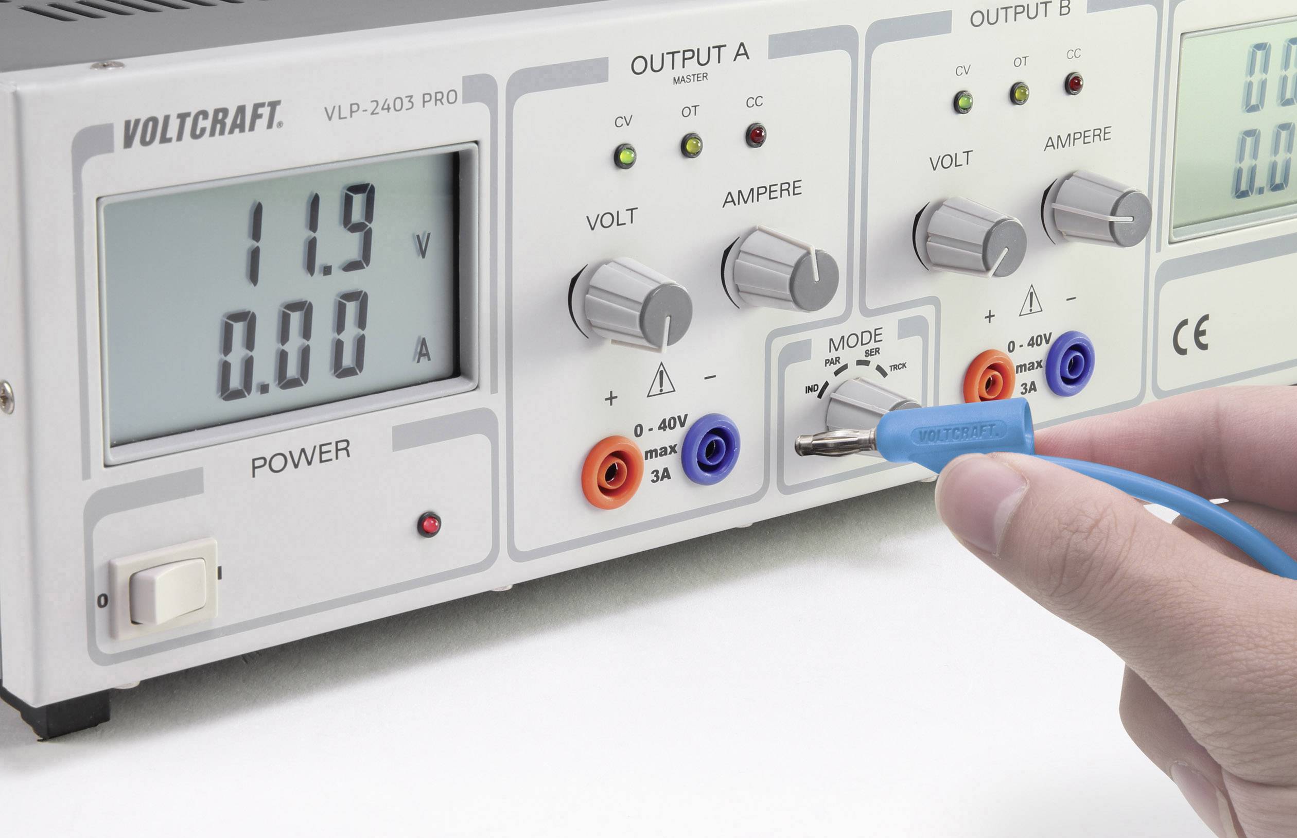 Ein Benutzer justiert ein Mehrkanal-Netzteil. Der Bildschirm zeigt 11,9 Volt und 0 Ampere an. Verschiedene Anschlüsse und Regler sind sichtbar.