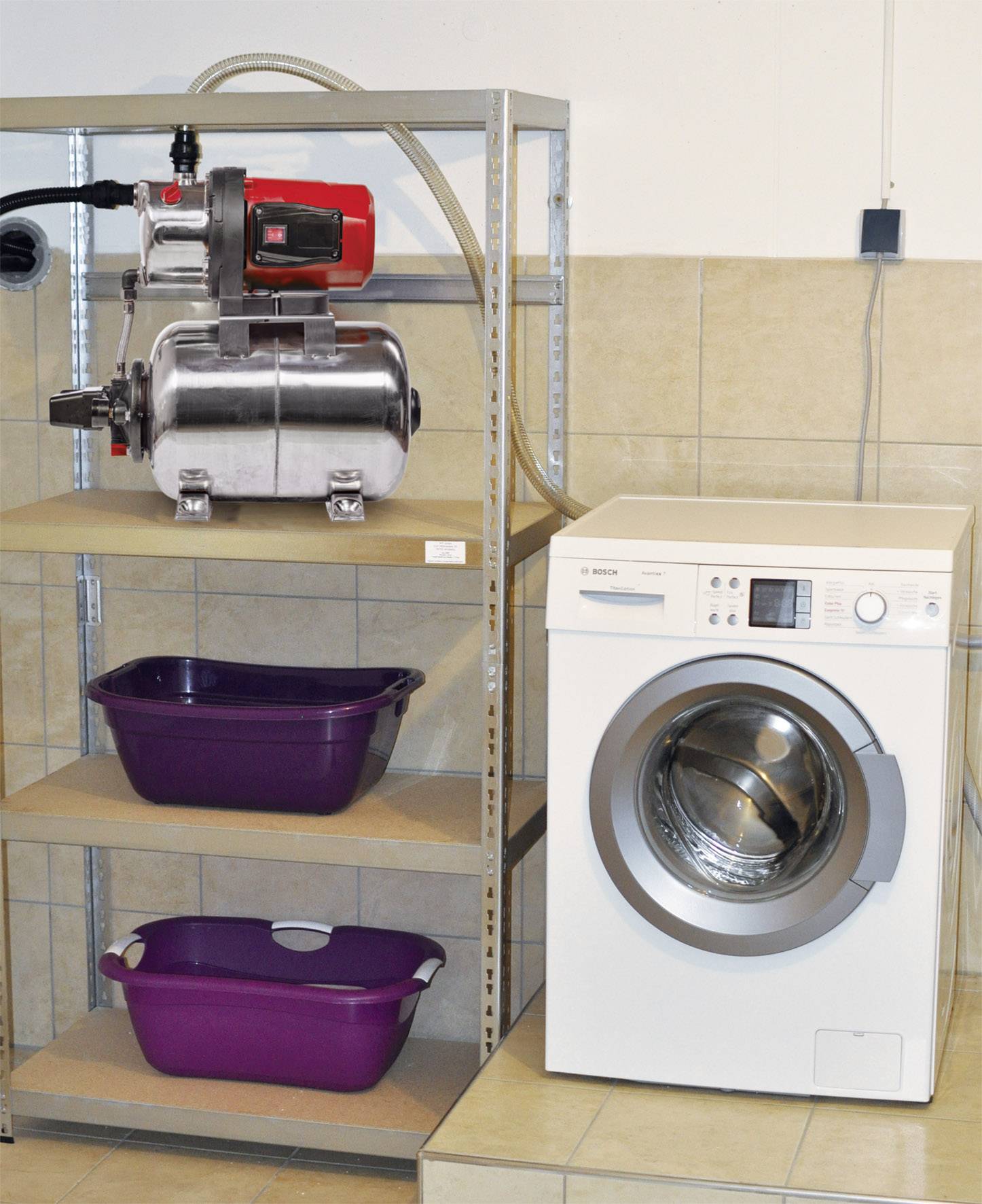 Eine weiße Waschmaschine steht neben einem Metallregal, auf dem sich eine Pumpe und zwei lila Wäscheschalen befinden.