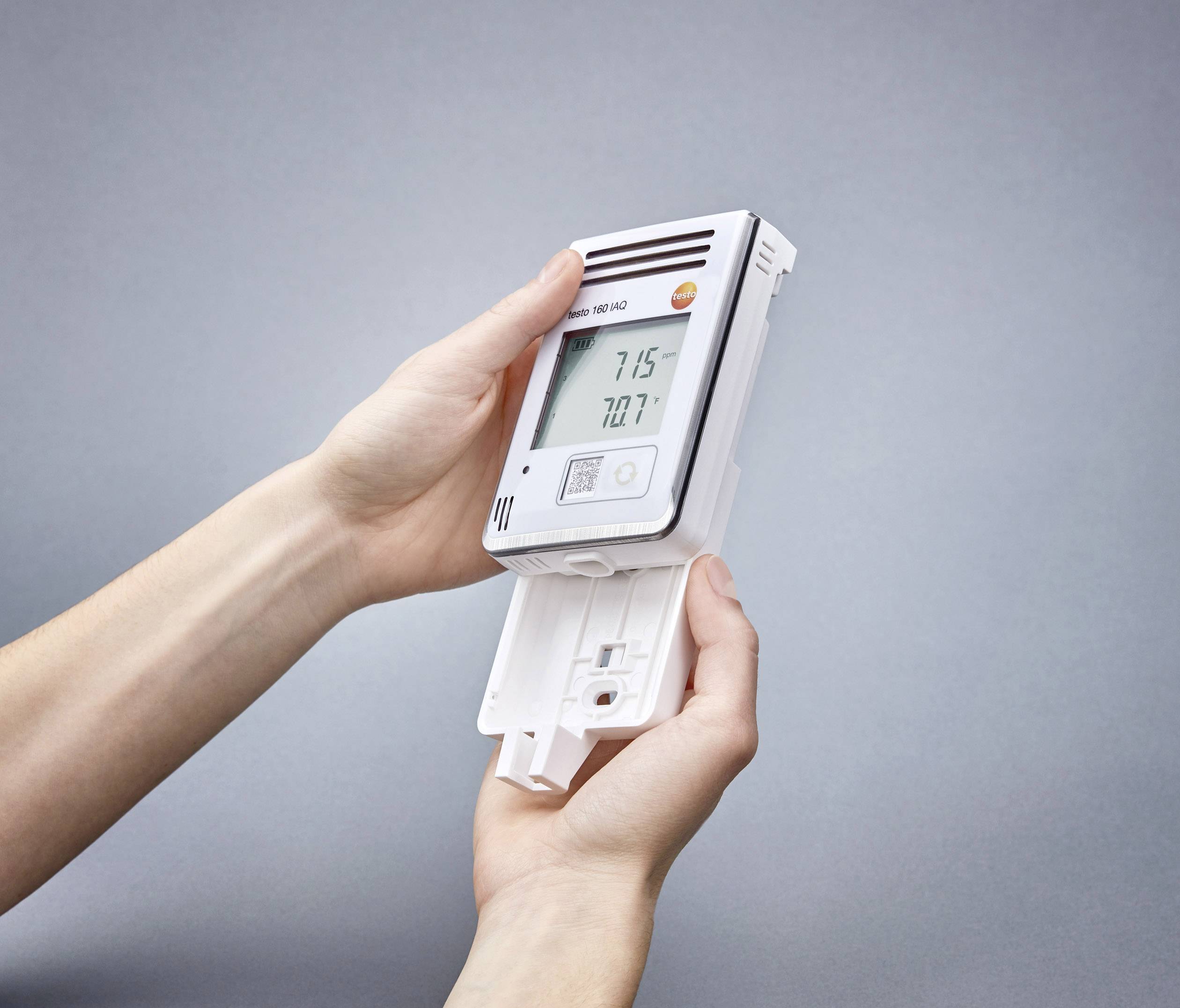 Hände halten ein digitales Gerät mit Display, das Temperaturen anzeigt. Das Gerät wird geöffnet, um einen Batteriewechsel vorzunehmen.