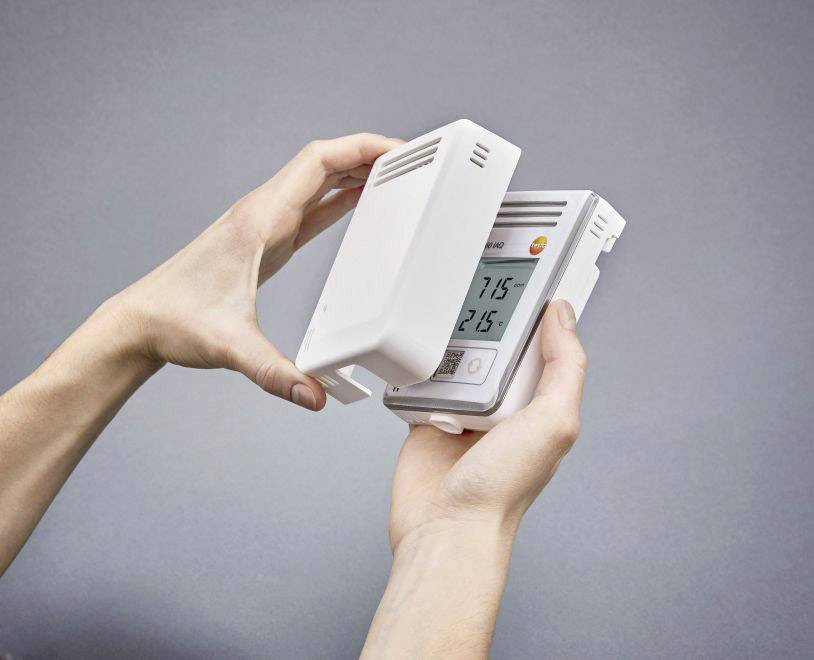 Eine Person hält ein Thermostat und öffnet das Gehäuse, um das Display anzuzeigen, auf dem '21.5' Grad Celsius steht.