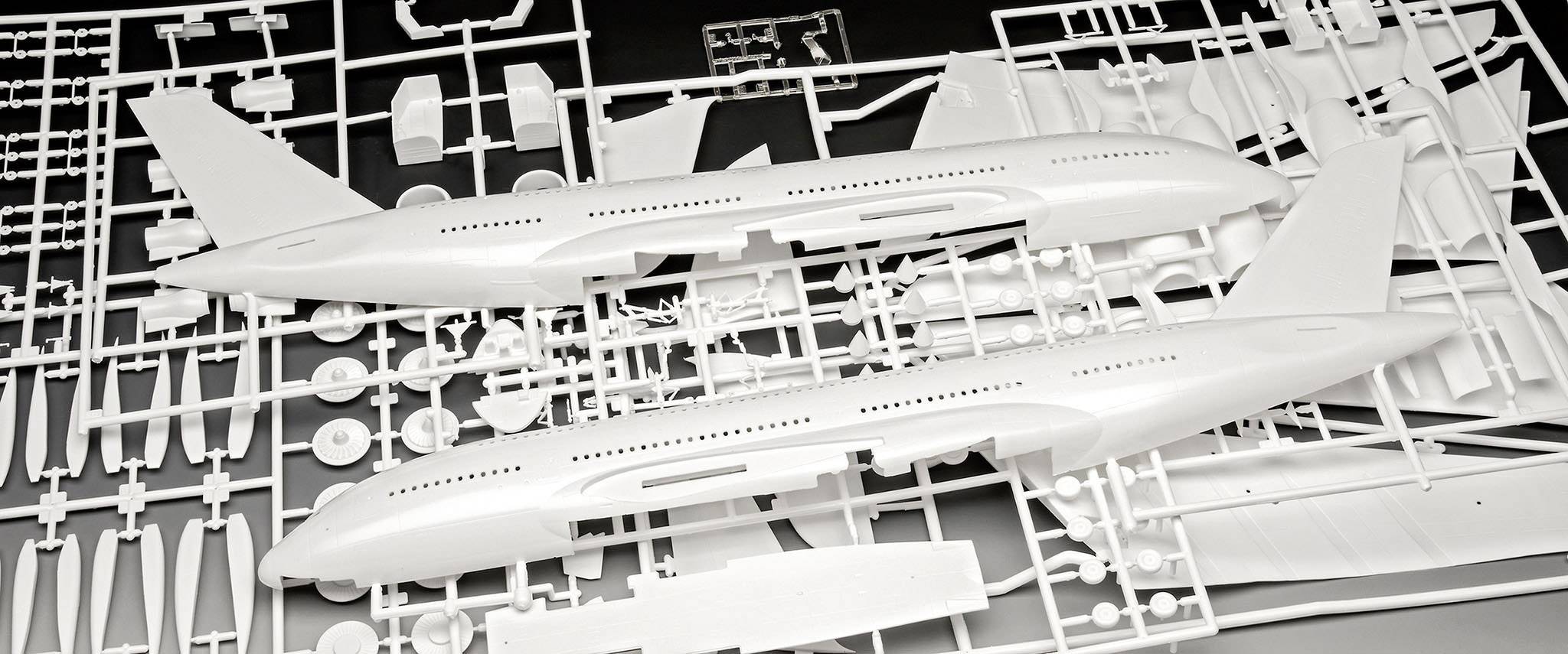 Zwei weiße Flugzeugmodell-Hälften auf einem durcheinander liegenden Modellbausatz mit verschiedenen kleineren Teilen und Rahmen.