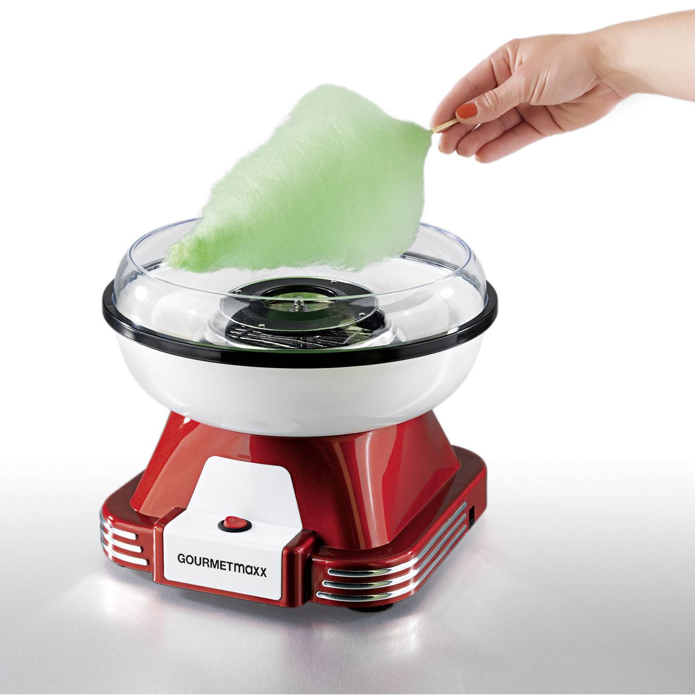 Eine Hand hält grünen Zuckerwattefaden, der aus einer roten und weißen Zuckerwattemaschine herauskommt.