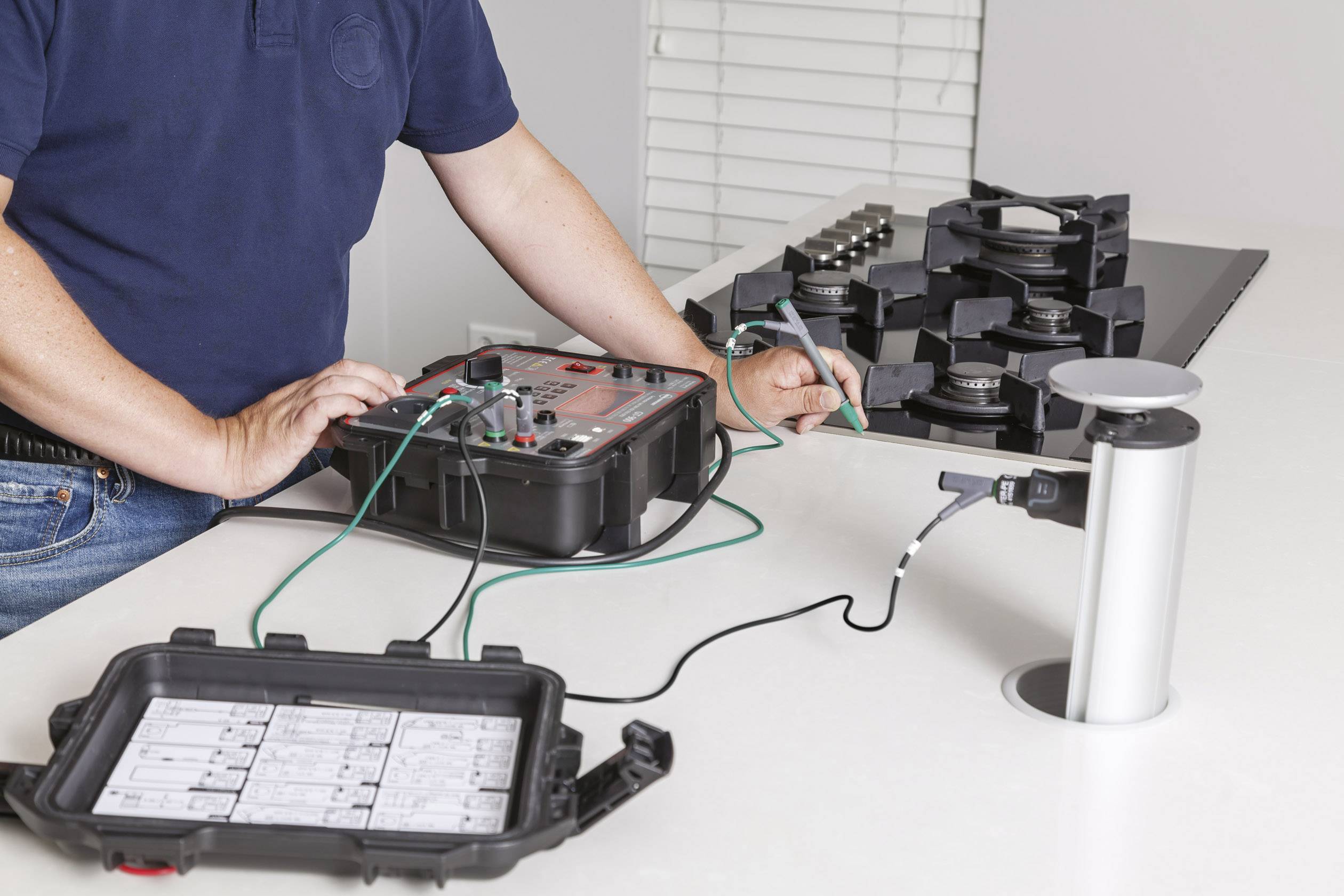 Eine Person führt Messungen an einem elektronischen Gerät durch, das mit Sensoren und Kabeln verbunden ist. Im Hintergrund sind Gewichte zu sehen.