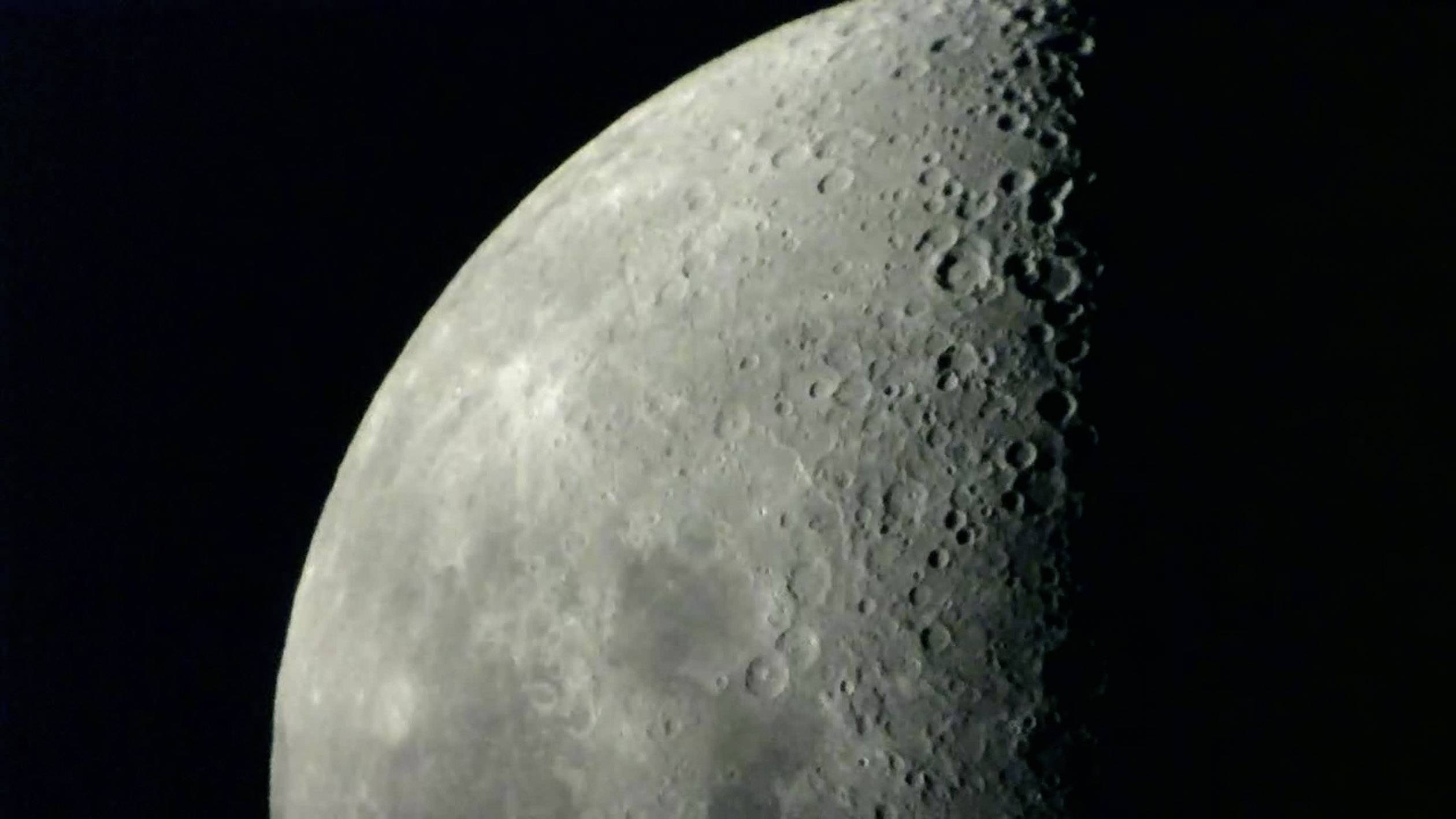 Halbmond mit sichtbaren Kratern und Oberflächenstrukturen bei Nacht.