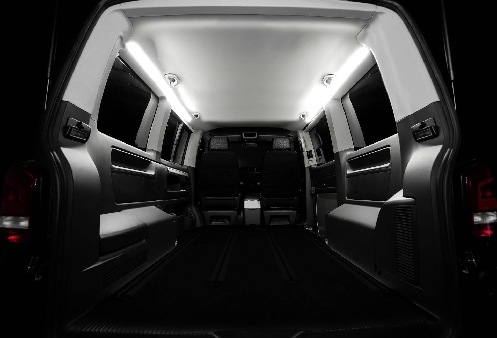 Der Innenraum eines leeren Transporters mit zwei Sitzen vorne, beleuchtet durch weiße LED-Leuchten entlang der Decke.