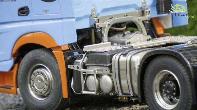 Nahaufnahme eines Modell-LKWs, der vorne hellblau und orange lackiert ist. Die Detailtreue der Metallteile und Reifen ist deutlich sichtbar.