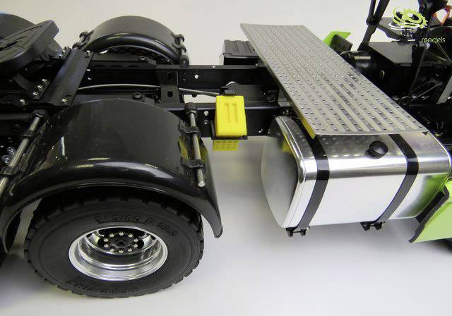 Nahaufnahme eines Lastwagen-Teils mit Ladefläche, großem Metalltank und schwarzem Rad. Hauptmerkmal: silberne Fläche mit gelben Details.