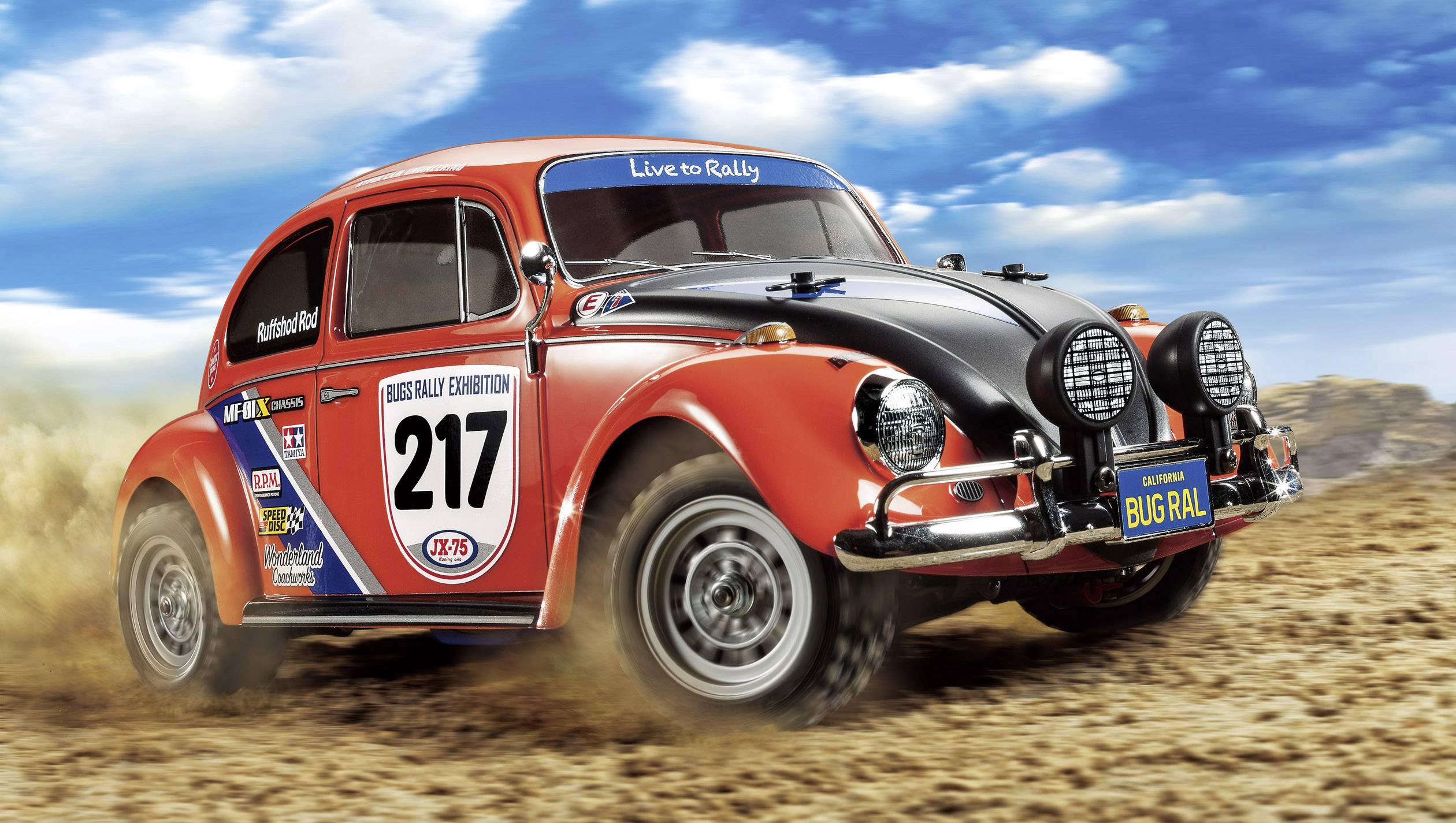 Ein roter Rallye-Käfer mit der Startnummer 217 fährt schnell über eine staubige Piste. Der Himmel ist blau und leicht bewölkt.